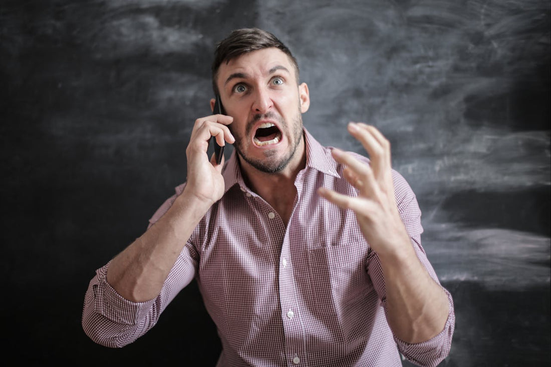 Frustrated man talking on the phone, appearing stressed and raising his hand in exasperation.