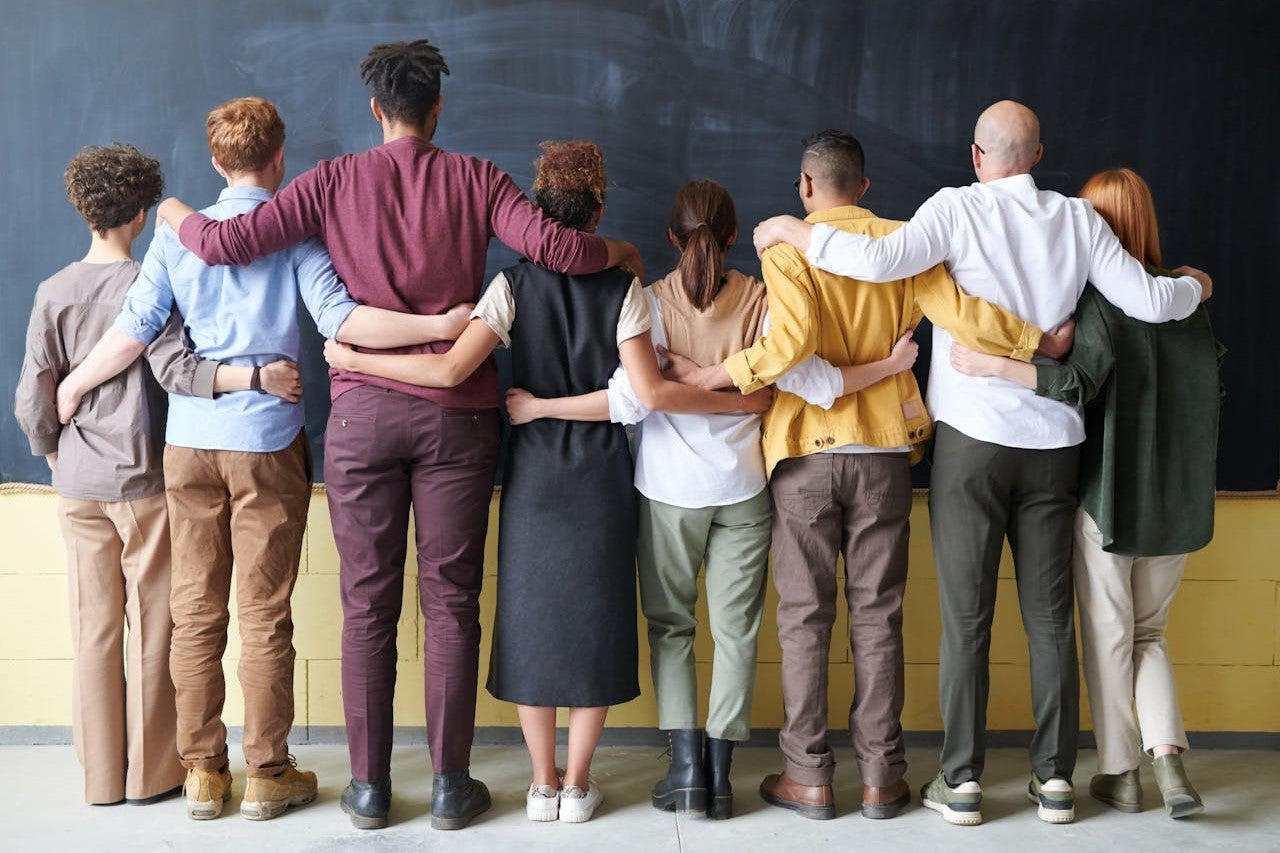 A diverse group of people standing with arms around each other.