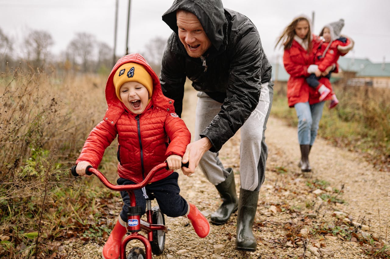 A father helping his young son ride a bicycle along a countryside path.