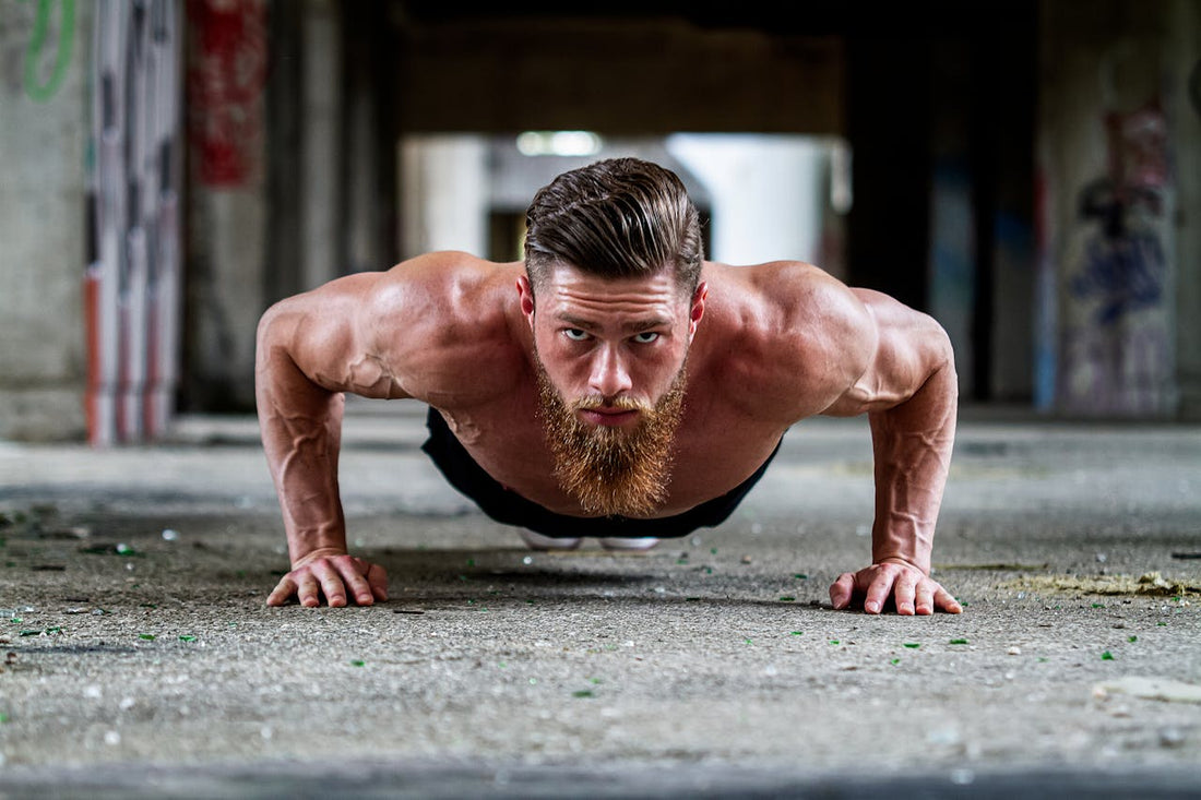 A muscular bearded man with a determined expression doing a push-up in an industrial setting, showcasing strength and fitness.