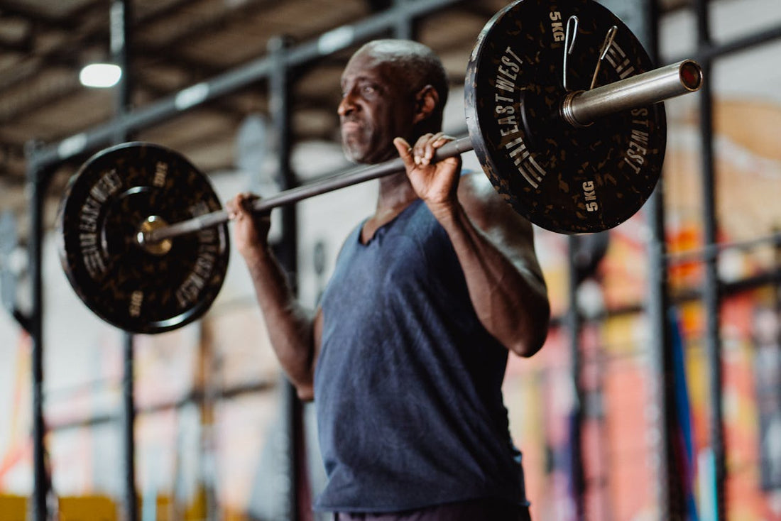 An older man lifting a barbell in a gym, demonstrating strength and fitness during a weightlifting exercise.