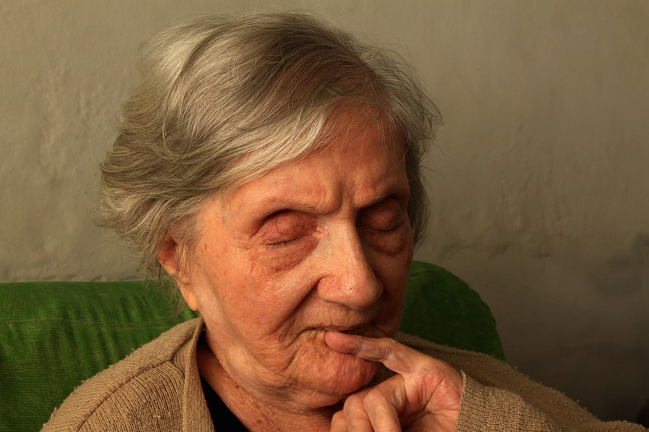 Elderly woman with closed eyes, resting while seated.