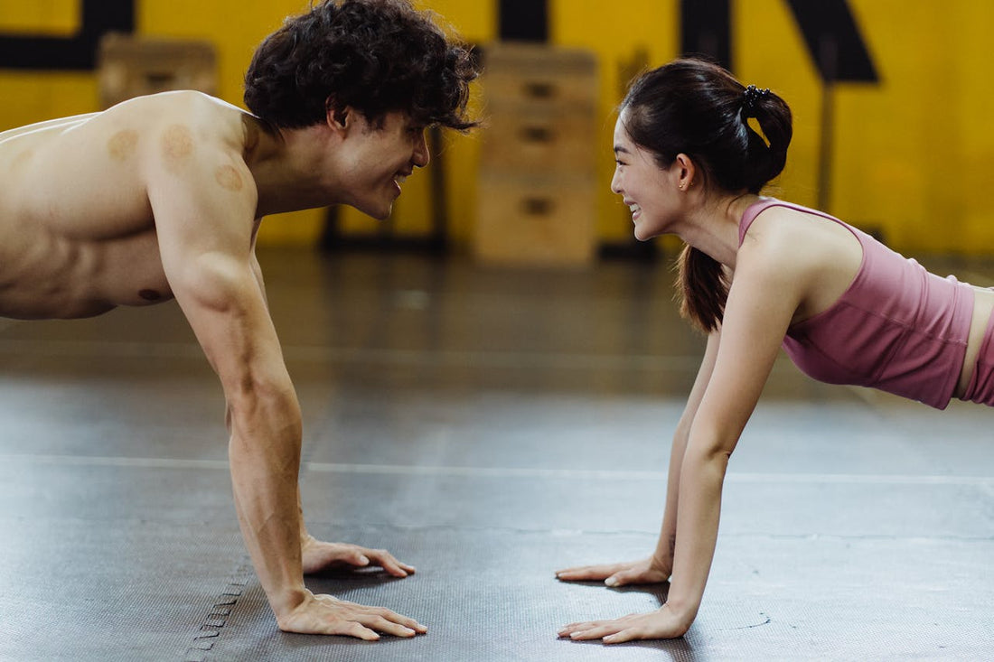 Man and woman smiling at each other while doing push-ups in a gym.
