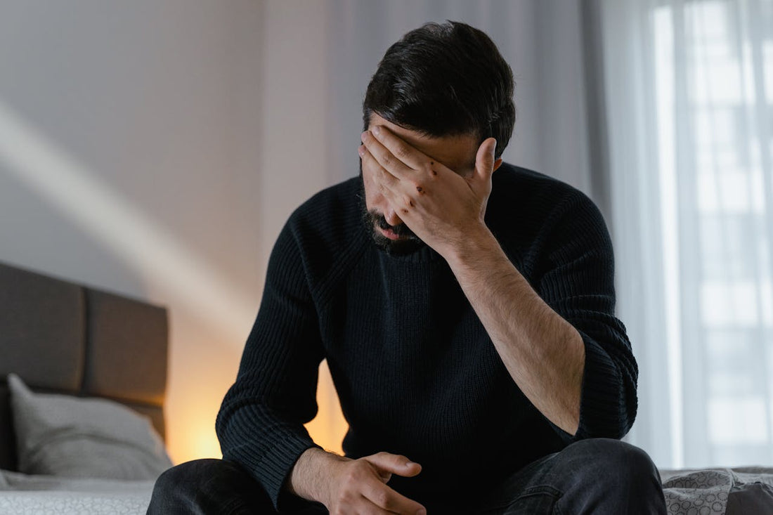Man sitting on the bed with his face in his hand, looking stressed and overwhelmed.