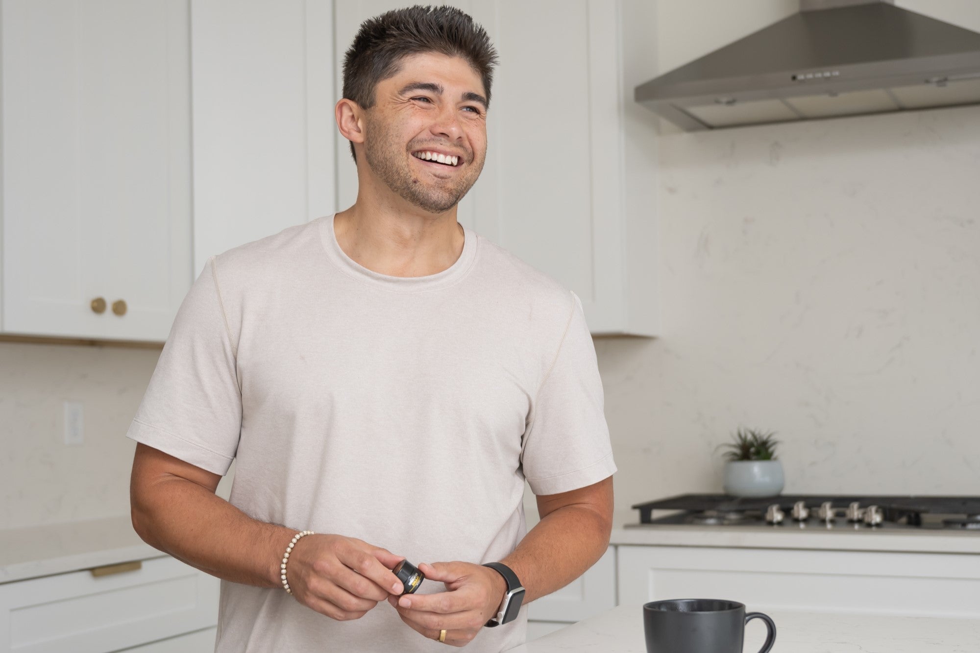 Smiling man holding a NutroTonic Shilajit resin jar in a modern kitchen.