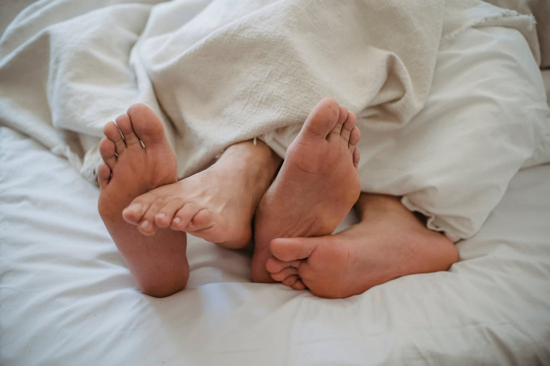 Two pairs of feet under white sheets, suggesting intimacy and connection between a couple.
